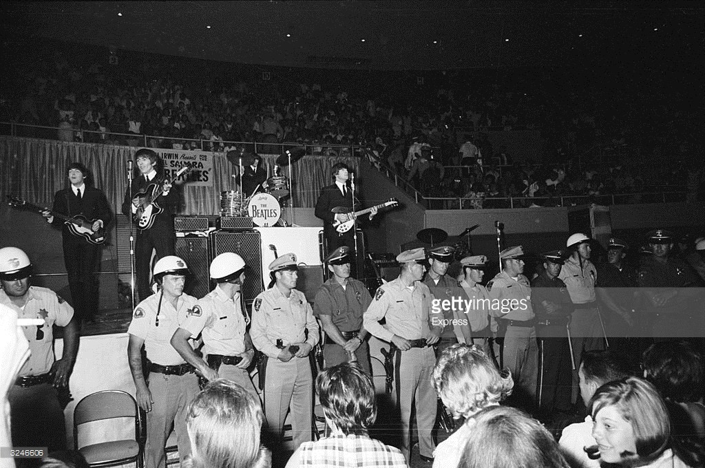A line of police officers prevent fans from getting too close, as The Beatles perform behind them on stage at the Convention Hall, Las Vegas.
