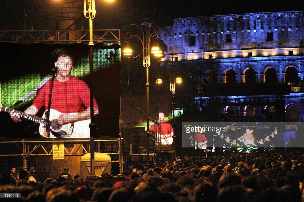 Shadowed by The Colosseum, Paul McCartney performs a free concert along the boulevard Via dei Fori Imperiali May 11, 2003 in Rome, Italy. The performance comes on the heels of another performed the night prior inside the Colosseum with profits going to Rome's archaeological offices and to Adopt-a-Minefield, the anti-landmines charity backed by McCartney and his wife.