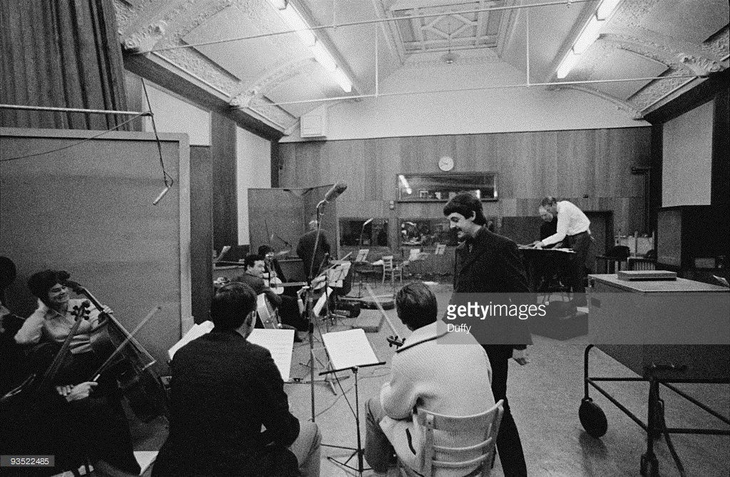 English singer, songwriter and musician Paul McCartney in a studio to record 'The Family Way', November 1966. At the back right, in a white shirt, is arranger and producer George Martin, and on the far left is cellist Therese Motard. Composed for the film of the same name, 'The Family Way' is considered by many to be the first Beatles solo album. A photoshoot for The Sunday Times.